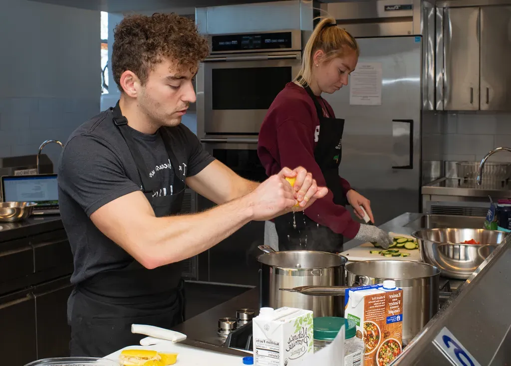 A nutrition student squeezes lemon into a pot in a large kitchen